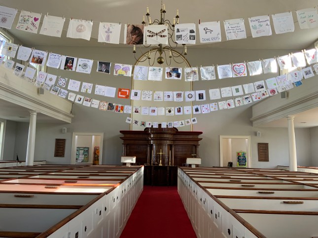 hand-decorated prayer flags stretch from balcony to balcony, high above the empty pews of a old New England church meetinghouse.